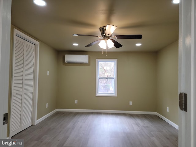 unfurnished bedroom featuring recessed lighting, a wall unit AC, baseboards, and wood finished floors