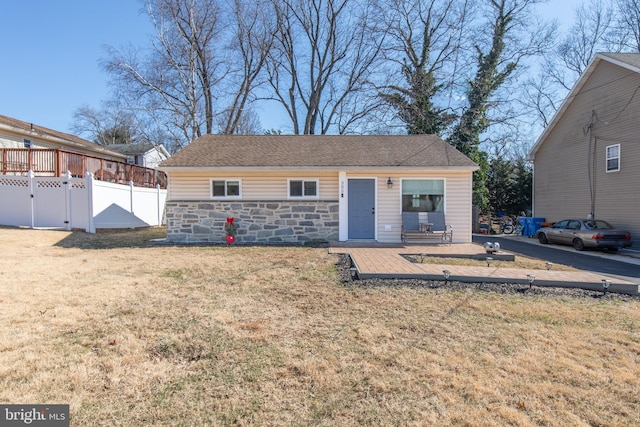 view of front of home featuring stone siding, a front lawn, and fence