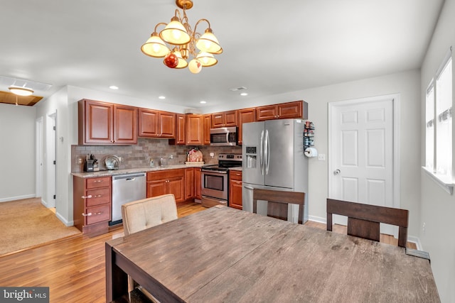 kitchen with a sink, decorative backsplash, hanging light fixtures, appliances with stainless steel finishes, and light wood-type flooring