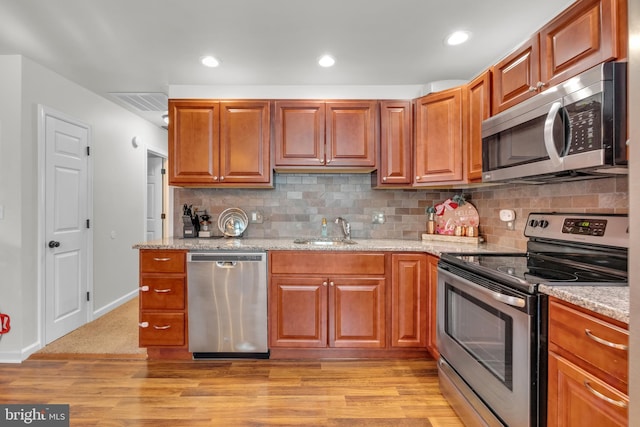 kitchen featuring light stone counters, light wood-style flooring, appliances with stainless steel finishes, and a sink