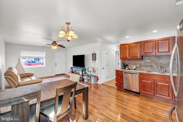 kitchen featuring backsplash, open floor plan, light wood-style floors, stainless steel appliances, and a sink