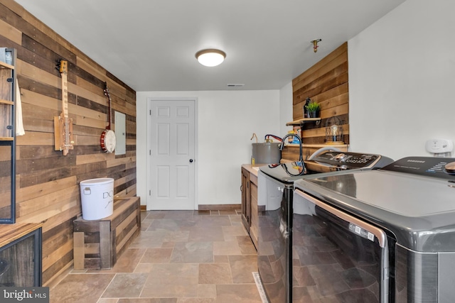 laundry room with stone finish floor, washing machine and dryer, laundry area, and wood walls