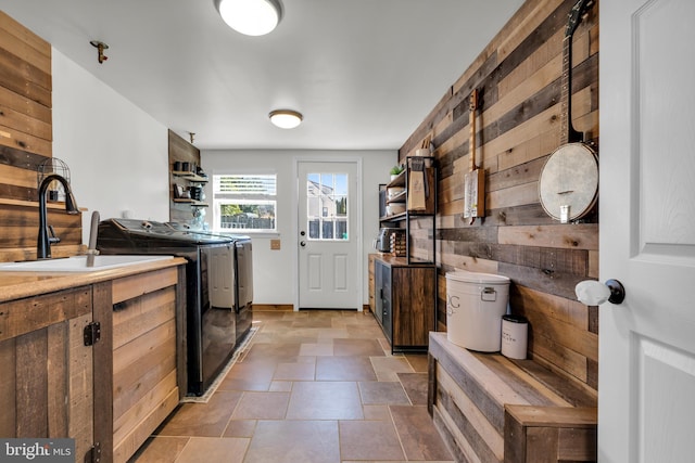 kitchen with open shelves, washer and clothes dryer, wood walls, stone finish floor, and a sink