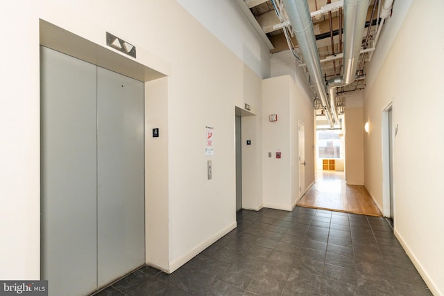 hallway featuring baseboards, elevator, and a high ceiling