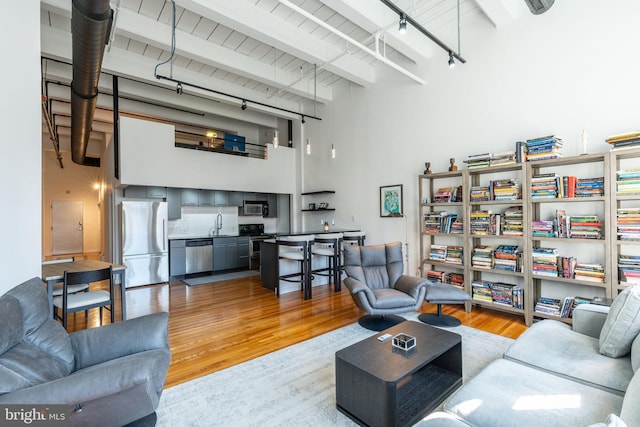 living room featuring beam ceiling, a towering ceiling, track lighting, and light wood finished floors