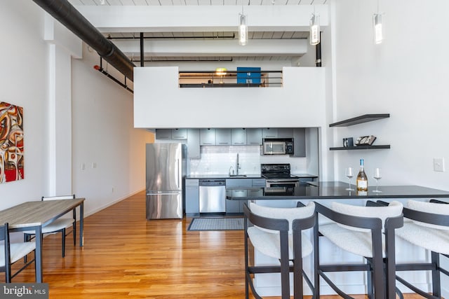 kitchen featuring dark countertops, beamed ceiling, decorative backsplash, light wood-style flooring, and appliances with stainless steel finishes