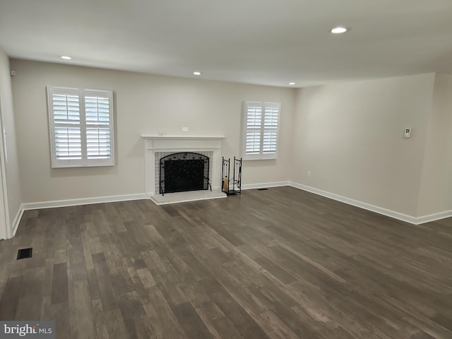 unfurnished living room with dark wood-type flooring, visible vents, recessed lighting, a brick fireplace, and baseboards