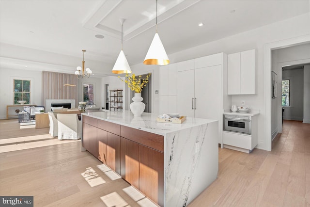 kitchen featuring a center island, white cabinets, light wood finished floors, and light stone countertops