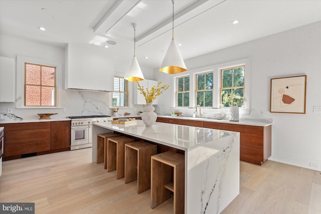 kitchen featuring brown cabinets, modern cabinets, light wood-style flooring, light stone countertops, and double oven range