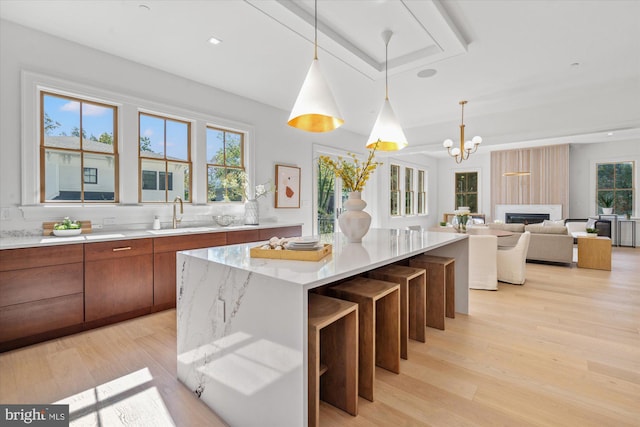 kitchen with a center island, decorative light fixtures, brown cabinetry, light wood-style floors, and a sink