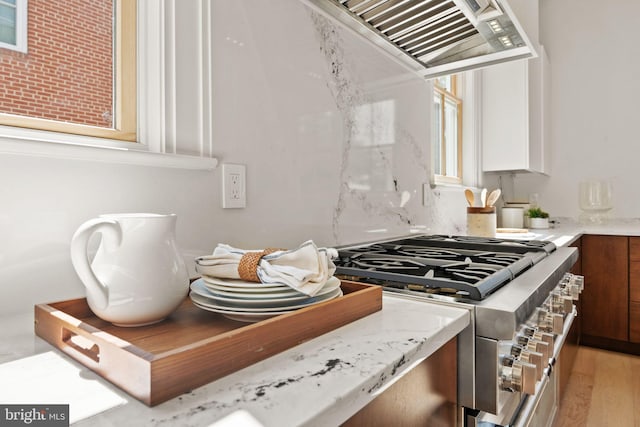 kitchen with light wood-type flooring, wall chimney exhaust hood, stainless steel gas range oven, and light stone countertops