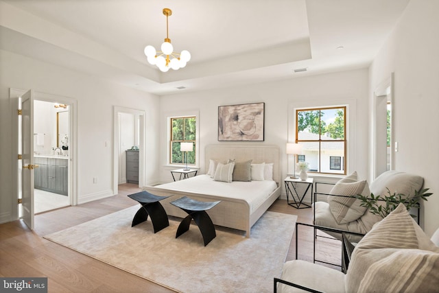 bedroom with light wood finished floors, multiple windows, a tray ceiling, and an inviting chandelier