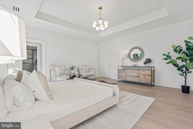 bedroom with light wood-style flooring, a raised ceiling, visible vents, and a notable chandelier