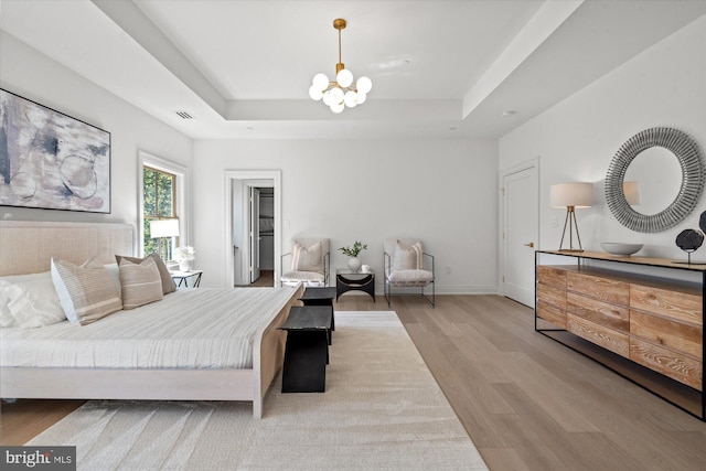 bedroom featuring wood finished floors, visible vents, baseboards, a tray ceiling, and an inviting chandelier