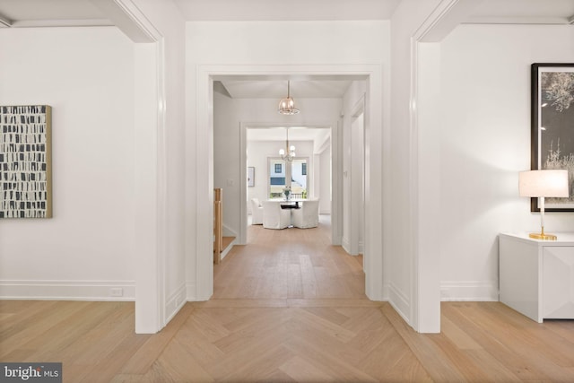 corridor with parquet floors, a notable chandelier, and baseboards