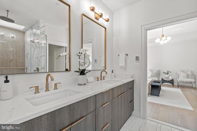 bathroom featuring marble finish floor, a sink, a tile shower, and double vanity