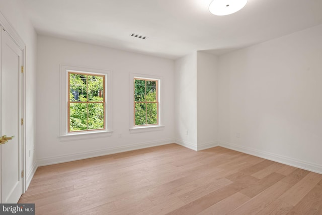 empty room with light wood-type flooring, visible vents, and baseboards