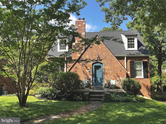 view of front of home featuring a chimney, brick siding, roof with shingles, and a front lawn