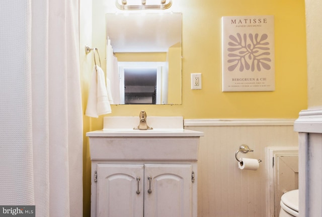 full bath featuring vanity, wainscoting, and toilet