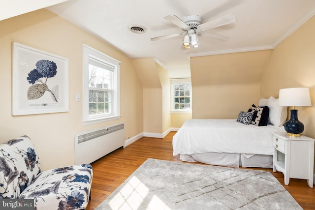 bedroom featuring a ceiling fan, wood finished floors, visible vents, baseboards, and radiator heating unit