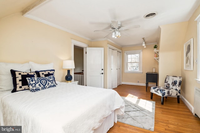 bedroom with a ceiling fan, wood finished floors, visible vents, baseboards, and crown molding