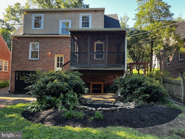 rear view of house with brick siding, stucco siding, fence, and a sunroom