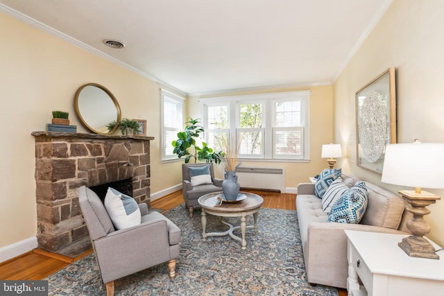 living area featuring visible vents, radiator, crown molding, a stone fireplace, and wood finished floors