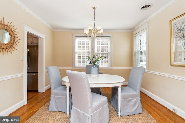 dining area with visible vents, light wood-style flooring, ornamental molding, baseboards, and a chandelier