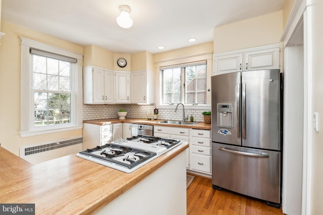 kitchen featuring wooden counters, radiator heating unit, appliances with stainless steel finishes, white cabinetry, and a sink