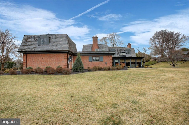 rear view of house featuring brick siding, a high end roof, a chimney, and a yard