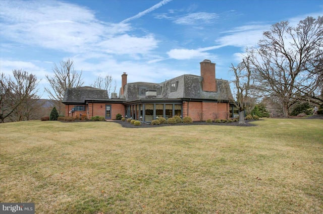 back of property featuring a sunroom, brick siding, a yard, and a chimney