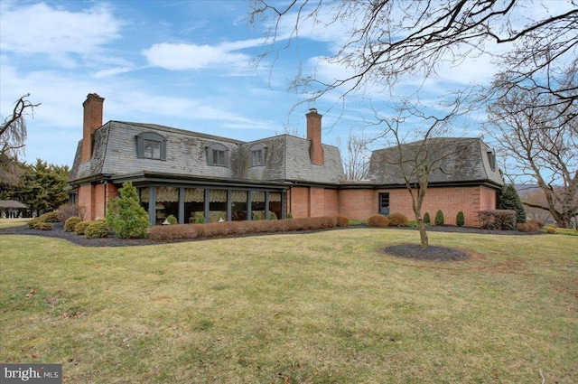 rear view of house with a yard, a chimney, and brick siding