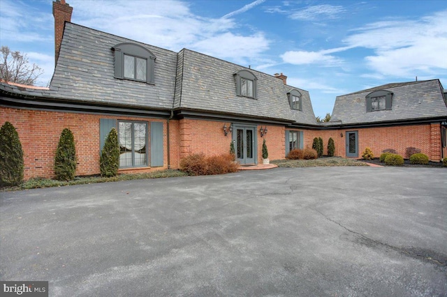 view of front of house with a high end roof, french doors, brick siding, and a chimney