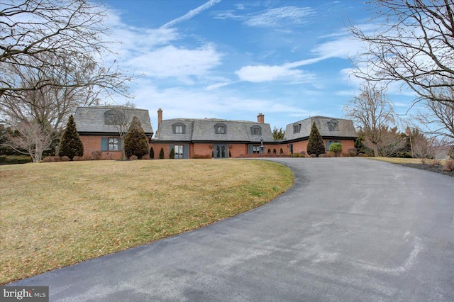 view of front of home with aphalt driveway, a front lawn, a chimney, and brick siding