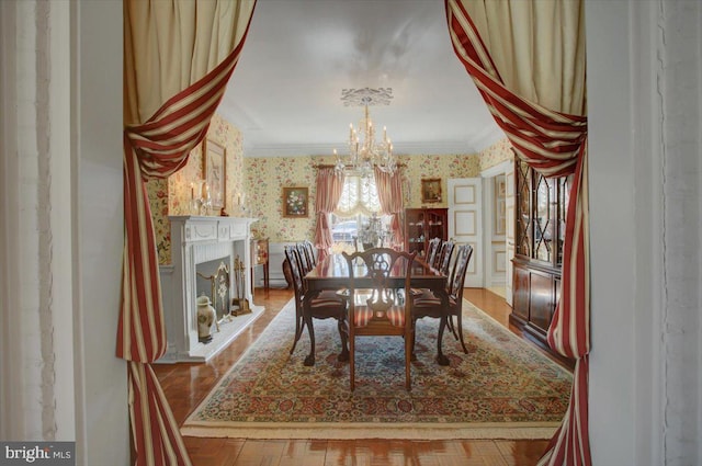 dining room featuring wallpapered walls, a notable chandelier, a fireplace, and crown molding