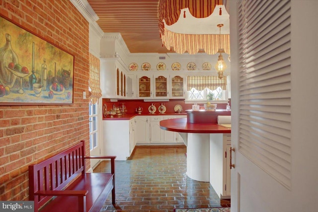 kitchen featuring brick floor, white cabinetry, glass insert cabinets, and brick wall