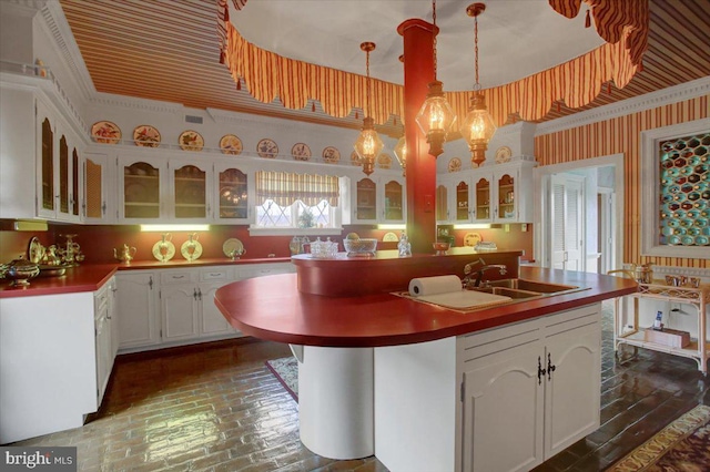 kitchen featuring brick floor, white cabinetry, an island with sink, glass insert cabinets, and wallpapered walls