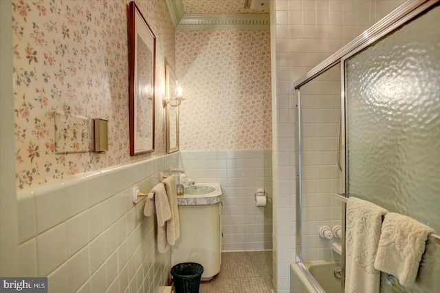 bathroom with wallpapered walls, a wainscoted wall, tile patterned flooring, combined bath / shower with glass door, and tile walls