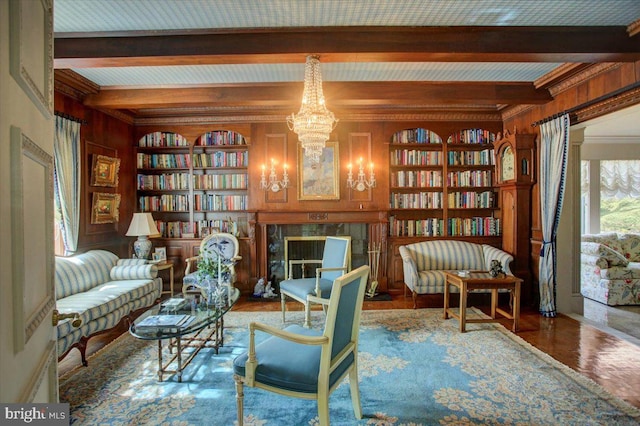 sitting room with beam ceiling, wood walls, built in shelves, a notable chandelier, and a high end fireplace