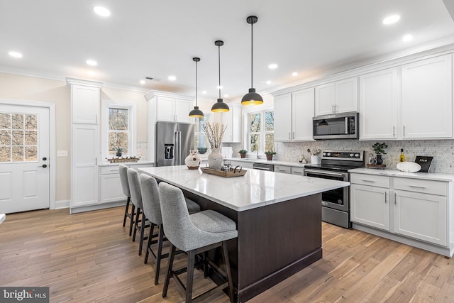 kitchen with decorative backsplash, ornamental molding, a center island, stainless steel appliances, and light wood-type flooring