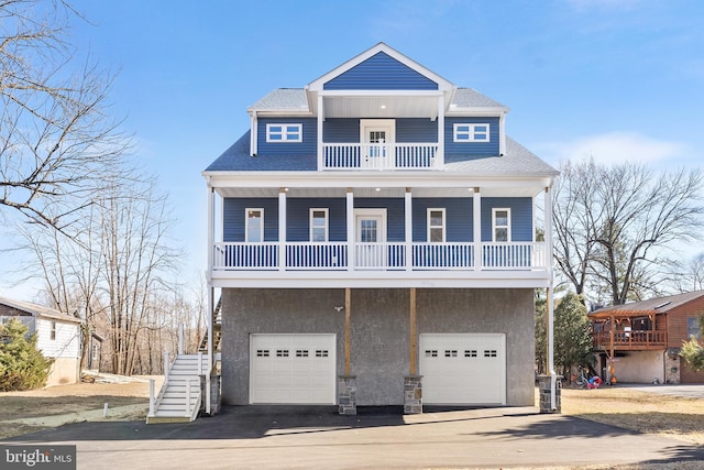 coastal home with roof with shingles, stucco siding, a balcony, driveway, and stairs