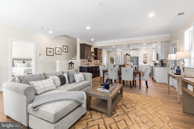 living room with light wood-style flooring, recessed lighting, visible vents, stairway, and crown molding