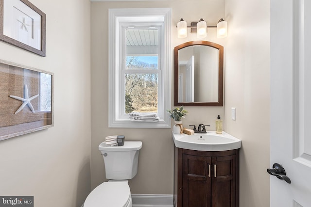 half bath with toilet, baseboards, and vanity