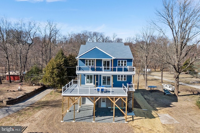 rear view of property featuring a balcony, driveway, a porch, and a shingled roof