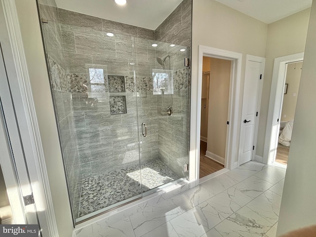 bathroom with marble finish floor, baseboards, a walk in closet, and a stall shower