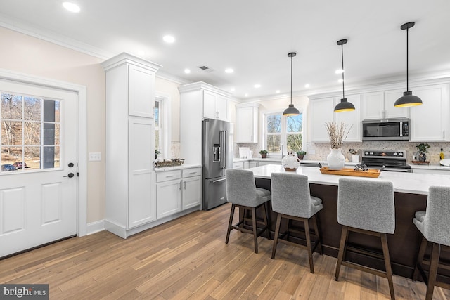 kitchen with appliances with stainless steel finishes, visible vents, ornamental molding, and a kitchen breakfast bar