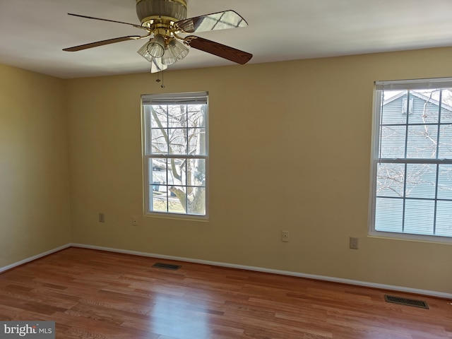 spare room featuring a wealth of natural light, visible vents, baseboards, and wood finished floors