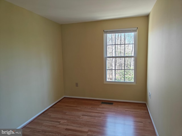 empty room with a wealth of natural light, visible vents, and wood finished floors