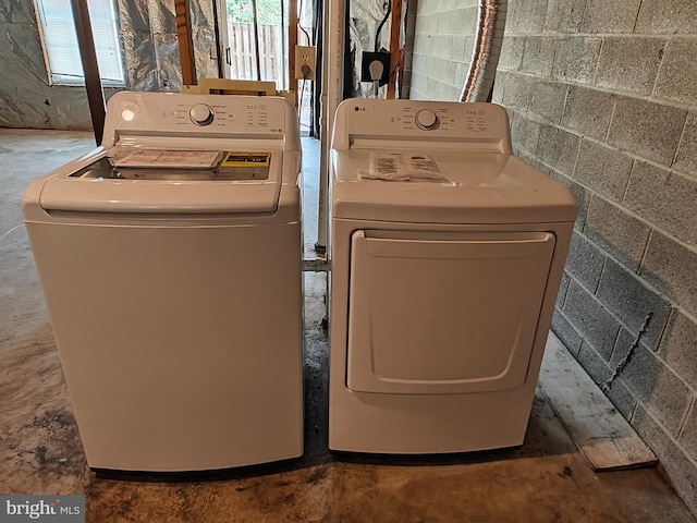 clothes washing area featuring concrete block wall, laundry area, and washer and clothes dryer