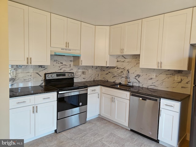 kitchen featuring appliances with stainless steel finishes, white cabinets, a sink, dark stone countertops, and under cabinet range hood